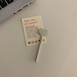 Pu&ograve; includere: Un cucchiaino d'argento a forma di cuore &egrave; appoggiato su una carta color crema con la scritta "Take care of yourself". La carta include consigli per la cura di s&eacute;. Una tastiera di un laptop &egrave; visibile sullo sfondo.