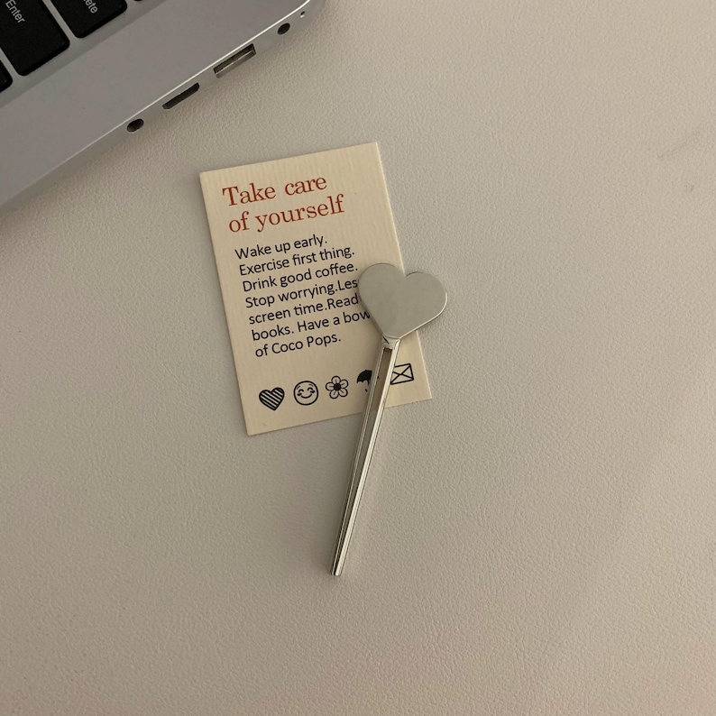 Pu&ograve; includere: Un cucchiaino d'argento a forma di cuore &egrave; appoggiato su una carta color crema con la scritta "Take care of yourself". La carta include consigli per la cura di s&eacute;. Una tastiera di un laptop &egrave; visibile sullo sfondo.