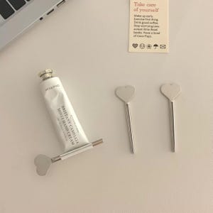 Puede incluir: Una taza de cerámica blanca con un asa negra y el texto "But First, Coffee" en negrita negra. La taza está sobre una superficie blanca. La taza mide 10 cm de alto.