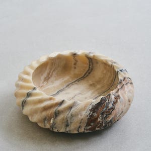 May include: A swirling, beige, brown and black marble bowl with a wavy, organic shape.