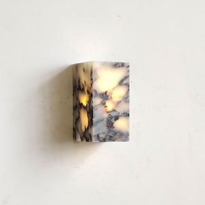 May include: A rectangular marble block with grey and white veining, illuminated from within. The light source emits a warm glow. This decorative lighting fixture is ideal for a modern interior. The dimensions are approximately 10 cm x 5 cm x 5 cm.