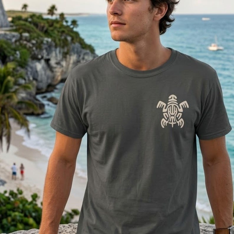 May include: A charcoal gray short-sleeve t-shirt featuring a cream-colored graphic of a stylized turtle on the left chest. The shirt has a crew neckline and a standard fit, constructed from a solid-colored fabric with a clean, simple design.