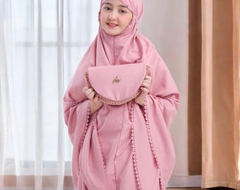 以下が含まれることがあります： 薄いピンク色の祈祷服。ヘッドカバーとそれに合うバッグが含まれています。バッグにはゴールドのチェーンストラップと装飾的なエンブレムが付いています。衣装にはスカラップレースのトリムが付いています。「GayatrArtID」の文字が右下にあります。