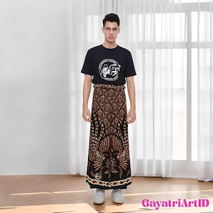 Puede incluir: Una persona con una camiseta negra con un gráfico blanco y un sarong batik marrón y negro. El sarong presenta un patrón detallado con elementos florales y geométricos. El atuendo se completa con zapatillas blancas.