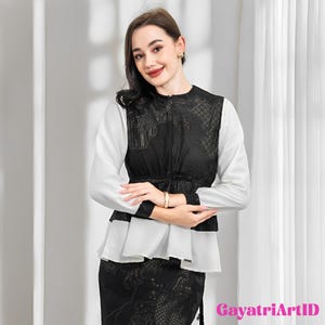 May include: A woman wearing a two-piece outfit. The top is a white blouse with long sleeves and a black lace overlay. The skirt is black with a matching lace pattern. The outfit is elegant and suitable for formal occasions.