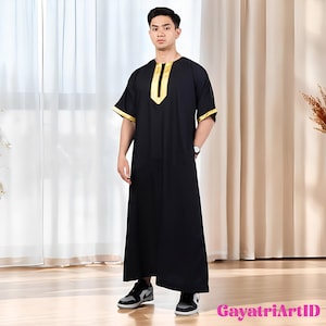 May include: Black thobe with gold trim on the neckline and sleeves. The long, loose-fitting garment is worn with black and gray sneakers. The image is set against a neutral background.
