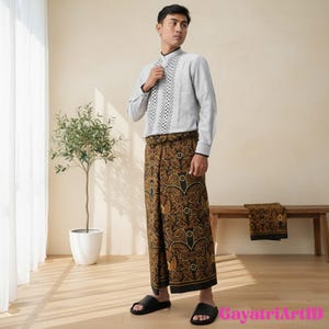 Puede incluir: Una persona vestida con una camisa gris claro de manga larga con un diseño estampado en blanco y negro en la parte delantera. La persona también lleva un sarong con estampado marrón y negro y sandalias negras. Un pequeño árbol en una maceta blanca está en el fondo.