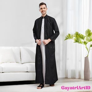Op de afbeelding: Een zwarte, lange mouwen jurk met een subtiel bloemmotief. De jurk wordt over een wit kledingstuk gedragen. De outfit wordt gecompleteerd met sandalen. De afbeelding bevat de tekst "GayatriArtID".