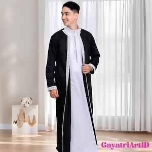 May include: A black and white traditional garment. The outer robe is black with silver trim along the edges and sleeves. The inner garment is white with a high collar and silver detailing. The outfit is worn by a person.