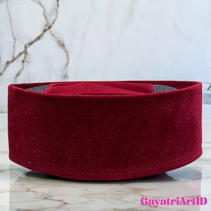 Könnte beinhalten: Eine bordeauxfarbene Samtkappe mit abgerundeter Krone und Mesh-Innenfutter. Die Kappe wird auf einer Marmoroberfläche präsentiert. Die Kappe ist eine traditionelle Kopfbedeckung.