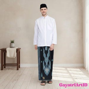 Könnte beinhalten: Eine Person trägt ein weißes Langarmhemd mit Stehkragen und einen Sarong mit schwarzem und blauem Muster. Die Person trägt auch eine schwarze Kappe. Das Bild wurde in Innenräumen aufgenommen.