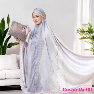 May include: A light purple prayer garment with a matching head covering, featuring a dotted and wavy pattern. The garment has a lace trim and is paired with a gray and pink rectangular bag. The background includes a white sofa and green plants.