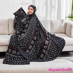 May include: A woman wearing a dark blue and brown patterned prayer garment, head covering, and pillow, sitting on a white sofa. The fabric features a geometric design with white accents. The text "GayatriArtID" is visible in the bottom right corner.