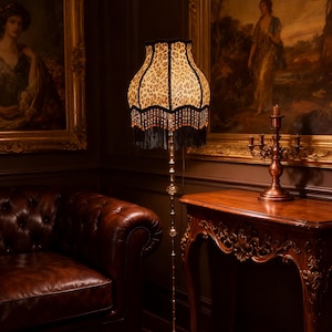 Può includere: Lampada da terra con paralume con stampa leopardata. Il paralume ha un bordo smerlato con frange nere e perline rosse. La lampada ha una base e uno stelo in metallo color oro. Lo sfondo comprende dipinti incorniciati, un divano in pelle e un tavolo di legno.