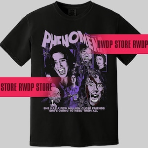 May include: Black t-shirt featuring a graphic from the movie "Phenomena" with a collage of faces and the text "She has a few million close friends, she's going to need them all." The design is in purple and white.