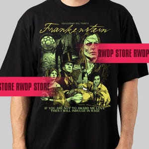 May include: Black t-shirt featuring a graphic from Guillermo del Toro's "Frankenstein." The design includes a collage of characters and the film's title in a stylized font. The quote "IF YOU ARE NOT TO AWARD ME LOVE THEN I WILL INDULGE IN RAGE" is also printed.