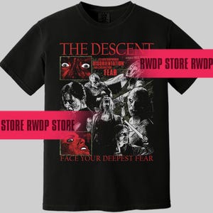 May include: Black t-shirt featuring a movie poster design for "The Descent." The design includes the movie title, imagery of terrified faces, and the phrase "Face Your Deepest Fear." The shirt is a classic crew neck style.