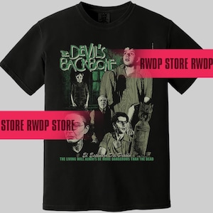 Könnte beinhalten: Schwarzes T-Shirt mit einem Filmplakat-Design für "The Devil's Backbone". Die Grafik enthält den Filmtitel in Grün, zusammen mit mehreren Figuren und dem Text "El Espinazo Del Diablo". Der Satz "Die Lebenden werden immer gefährlicher sein als die Toten" ist ebenfalls vorhanden.