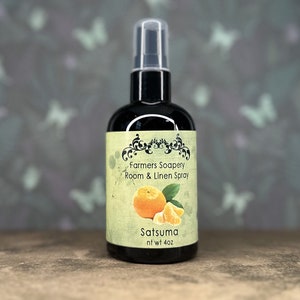 May include: A black glass bottle with a spray nozzle, labeled "Farmers Soapery Room & Linen Spray" and "Satsuma" with a picture of a mandarin orange. The bottle is 4 oz.