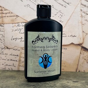 May include: A black bottle of Farmers Soapery hand and body lotion with a blue and white label. The label features a stylized image of a woman standing between three moons. The text on the label reads "Farmers Soapery Hand & Body Lotion" and "Summer Moon" with a net weight of 4 oz.