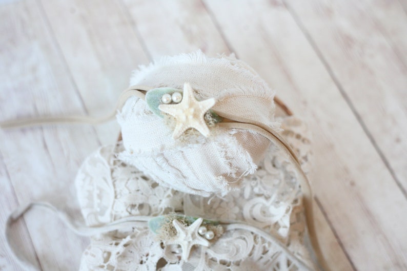 May include: A white headband with a beige ribbon and a starfish with pearl accents.