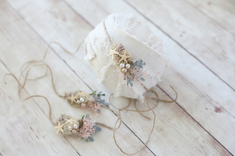 K&ouml;nnte beinhalten: Ein Set aus zwei Baby-Stirnb&auml;ndern f&uuml;r Neugeborene mit rustikalem, nat&uuml;rlichem Thema. Jedes Stirnband ist mit einem kleinen Strau&szlig; aus Kunstblumen, Perlen und goldenen Sternchen verziert. Die Stirnb&auml;nder sind mit einem braunen Bindfaden gebunden.