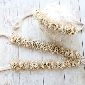 May include: A set of two cream-colored crocheted headbands with dried white flowers. The headbands are tied with a cream-colored ribbon.