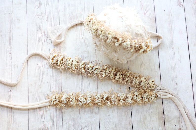 May include: A set of two cream-colored crocheted headbands with dried white flowers. The headbands are tied with a cream-colored ribbon.