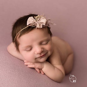 May include: A newborn baby girl is sleeping on a pink blanket. She is wearing a headband with a flower and a bow.