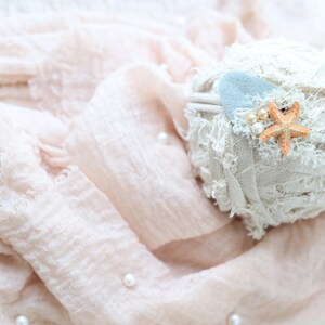 May include: A white fabric headband with a light blue felt starfish and a small orange starfish. The headband is on a pink fabric background.