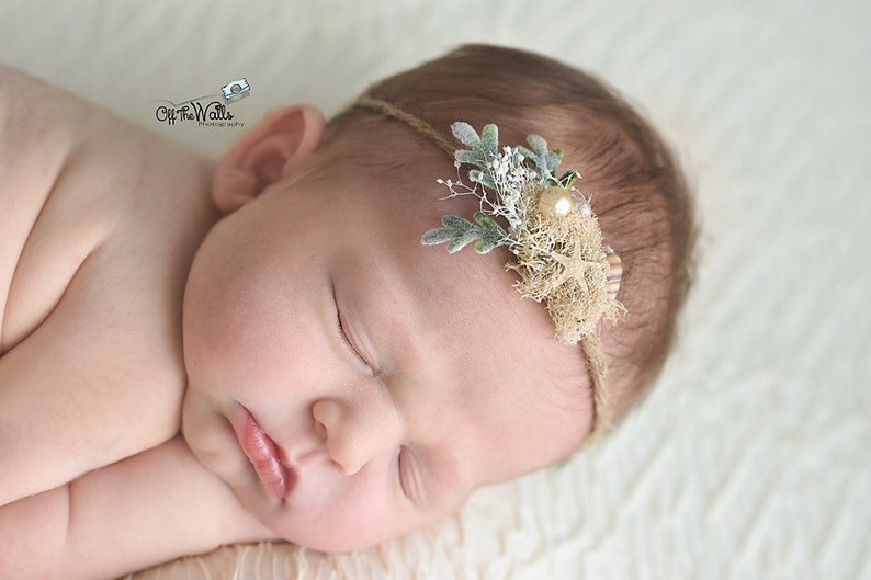 K&ouml;nnte beinhalten: Ein neugeborenes Baby-M&auml;dchen schl&auml;ft mit einem braunen und wei&szlig;en Blumen-Stirnband mit einem Perlen-Akzent.