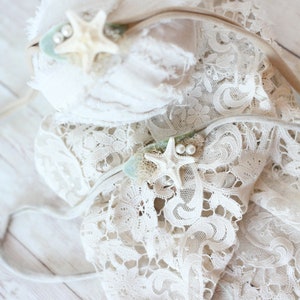 May include: Two white lace headbands with starfish and pearl accents. The headbands are on a white wooden background.