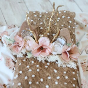 May include: A brown and white knitted blanket with a floral crown and gold antlers on top. The blanket has a textured surface with white polka dots.