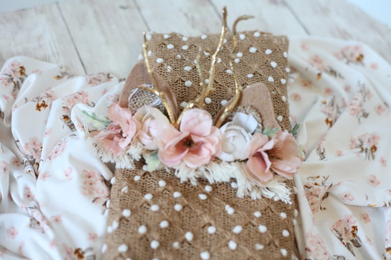 May include: A brown and white knitted blanket with a floral crown and gold antlers on top. The blanket has a textured surface with white polka dots.