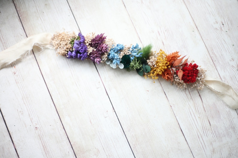 Puede incluir: Una guirnalda de flores secas de colores arco&iacute;ris con una cinta blanca. La guirnalda presenta flores moradas, azules, verdes, amarillas, naranjas y rojas.