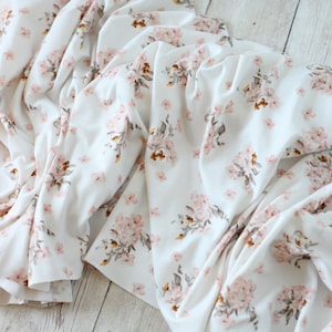 May include: White fabric with a pink and brown floral pattern. The fabric is folded and wrinkled.