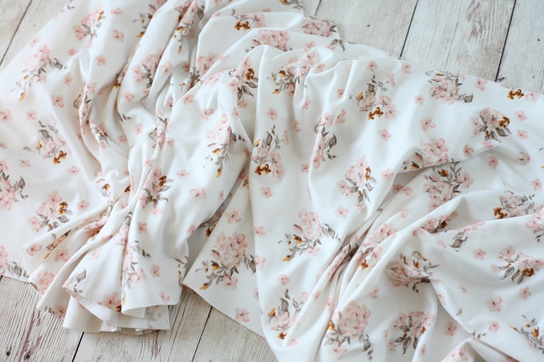 May include: White fabric with a pink and brown floral pattern. The fabric is folded and wrinkled.