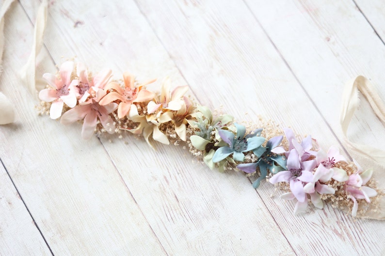 K&ouml;nnte beinhalten: Eine pastellfarbene Blumenkrone mit einem wei&szlig;en Satinband. Die Krone hat einen Farbverlauf von Rosa bis Blau.