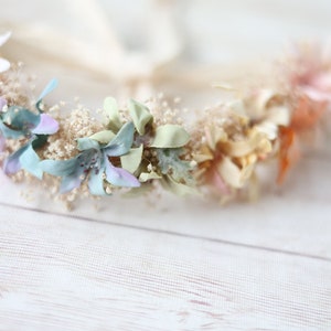 K&ouml;nnte beinhalten: Eine zarte Blumenkrone mit pastellfarbenen Bl&uuml;ten, darunter hellblau, Lavendel, Rosa und Creme, auf einem wei&szlig;en Hintergrund arrangiert.