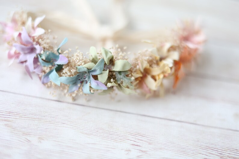 K&ouml;nnte beinhalten: Eine zarte Blumenkrone mit pastellfarbenen Bl&uuml;ten, darunter hellblau, Lavendel, Rosa und Creme, auf einem wei&szlig;en Hintergrund arrangiert.