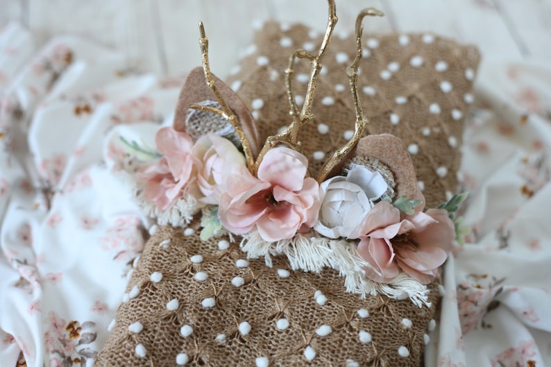 May include: A brown burlap fabric with white polka dots and a gold twig headband with pink and white flowers. The headband has a fringe trim.