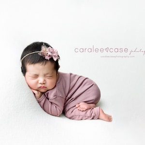 May include: A newborn baby girl is sleeping on a white background. She is wearing a pink knitted outfit and a headband with a pink flower. The text "caralee&hearts;case photography" is visible in the upper right corner of the image.