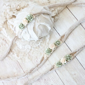 May include: Two beige fabric headbands with green and cream fabric flowers. The headbands are on a white wooden surface.