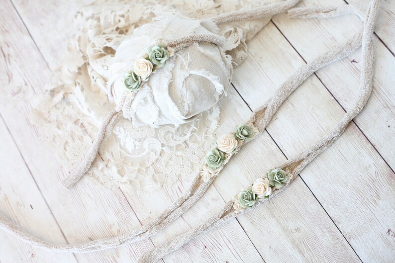 May include: Two beige fabric headbands with green and cream fabric flowers. The headbands are on a white wooden surface.