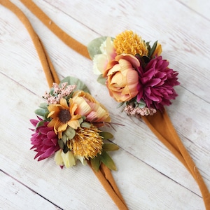 Può includere: Due fasce elastiche marroni con decorazioni floreali. I fiori sono un mix di giallo, arancione e bordeaux.