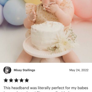 Puede incluir: Una ni&ntilde;a peque&ntilde;a con una diadema de flores arco&iacute;ris pastel, un vestido blanco con lunares dorados y un pastel blanco con glaseado blanco. La beb&eacute; est&aacute; sentada frente a un fondo de globos pastel.