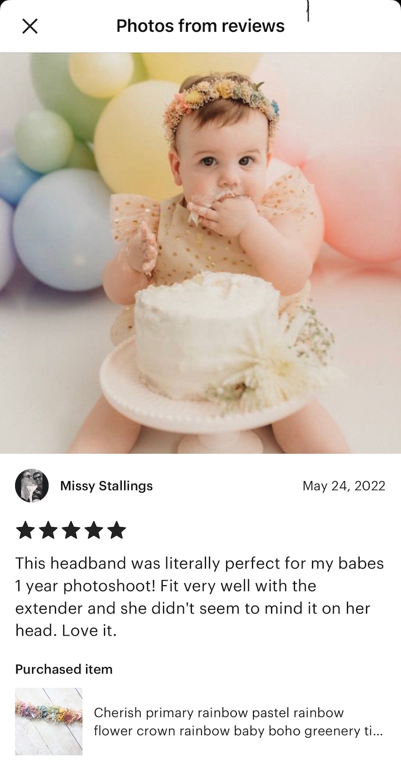 Puede incluir: Una ni&ntilde;a peque&ntilde;a con una diadema de flores arco&iacute;ris pastel, un vestido blanco con lunares dorados y un pastel blanco con glaseado blanco. La beb&eacute; est&aacute; sentada frente a un fondo de globos pastel.