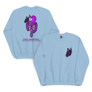 May include: Light blue sweatshirt with a purple butterfly on the front and back. The back features a purple illustration of the digestive system with a butterfly and the text "SMAS Awareness". The sleeve has a small blue ribbon graphic.