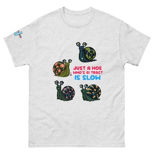 May include: Light gray t-shirt featuring four cartoon snails with patterned shells. The text "JUST A HOE WHO'S GI TRACT IS SLOW" is printed in pink, blue, and white. The shirt has a classic crew neck and short sleeves.