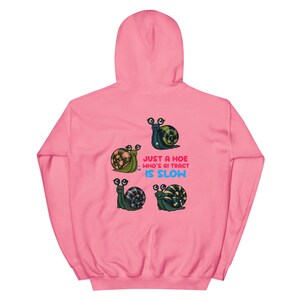 May include: Pink hooded sweatshirt featuring four cartoon snails with googly eyes. The snails have colorful shells and are arranged around the text "JUST A HOE WHO'S GI TRACT IS SLOW" in blue and pink.